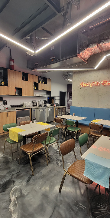 Modern small restaurant interior with wooden tables, mixed chairs, blue bench seating, and kitchen area.