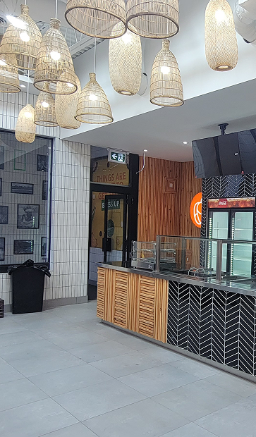 Modern café interior with hanging basket lights, tiled counter, and a Coca-Cola fridge.
