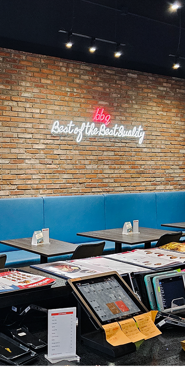 Modern BBQ restaurant interior with brick wall, neon sign, blue seating, tables, menus, and POS system.
