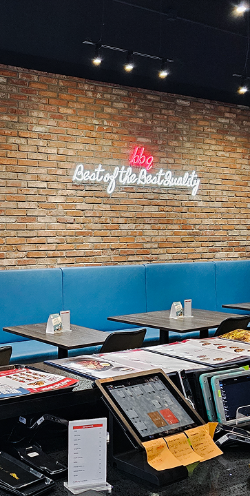 Restaurant interior with brick wall, neon sign reading bbq best quality, tables, and POS system.