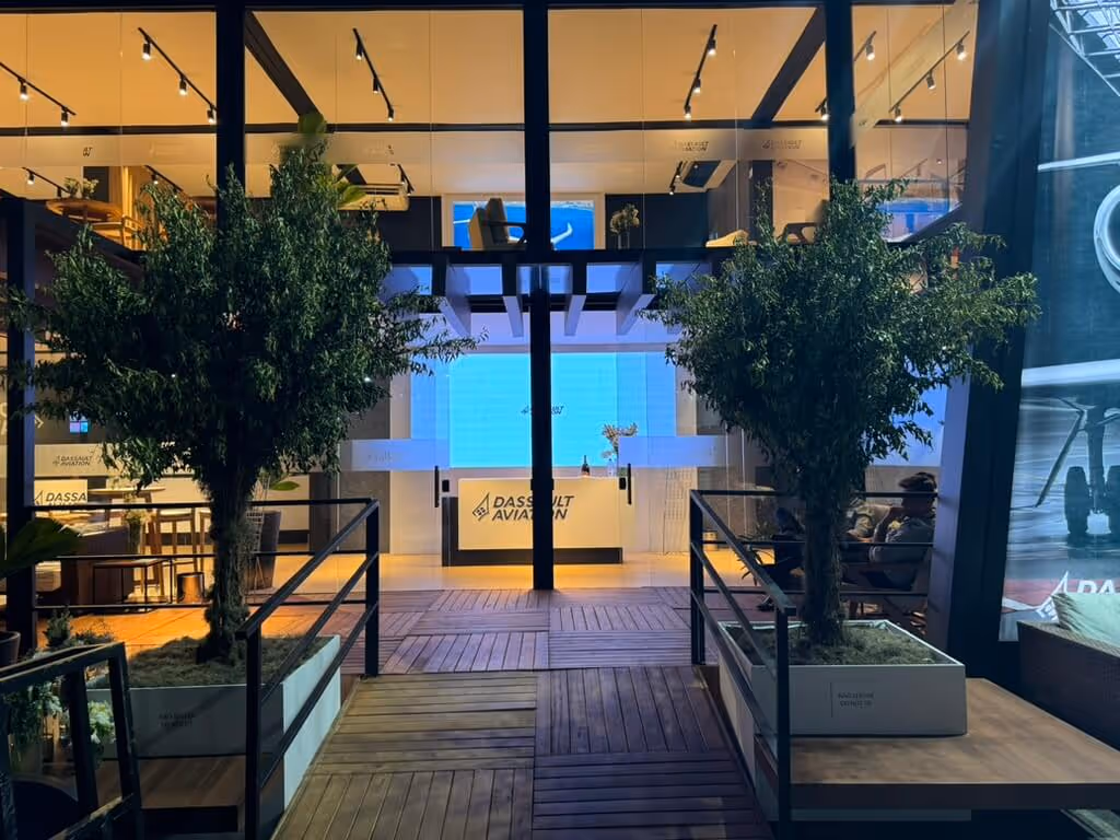 Modern Dassault Aviation office entrance with wooden flooring, two large potted trees, glass walls, and illuminated interior.