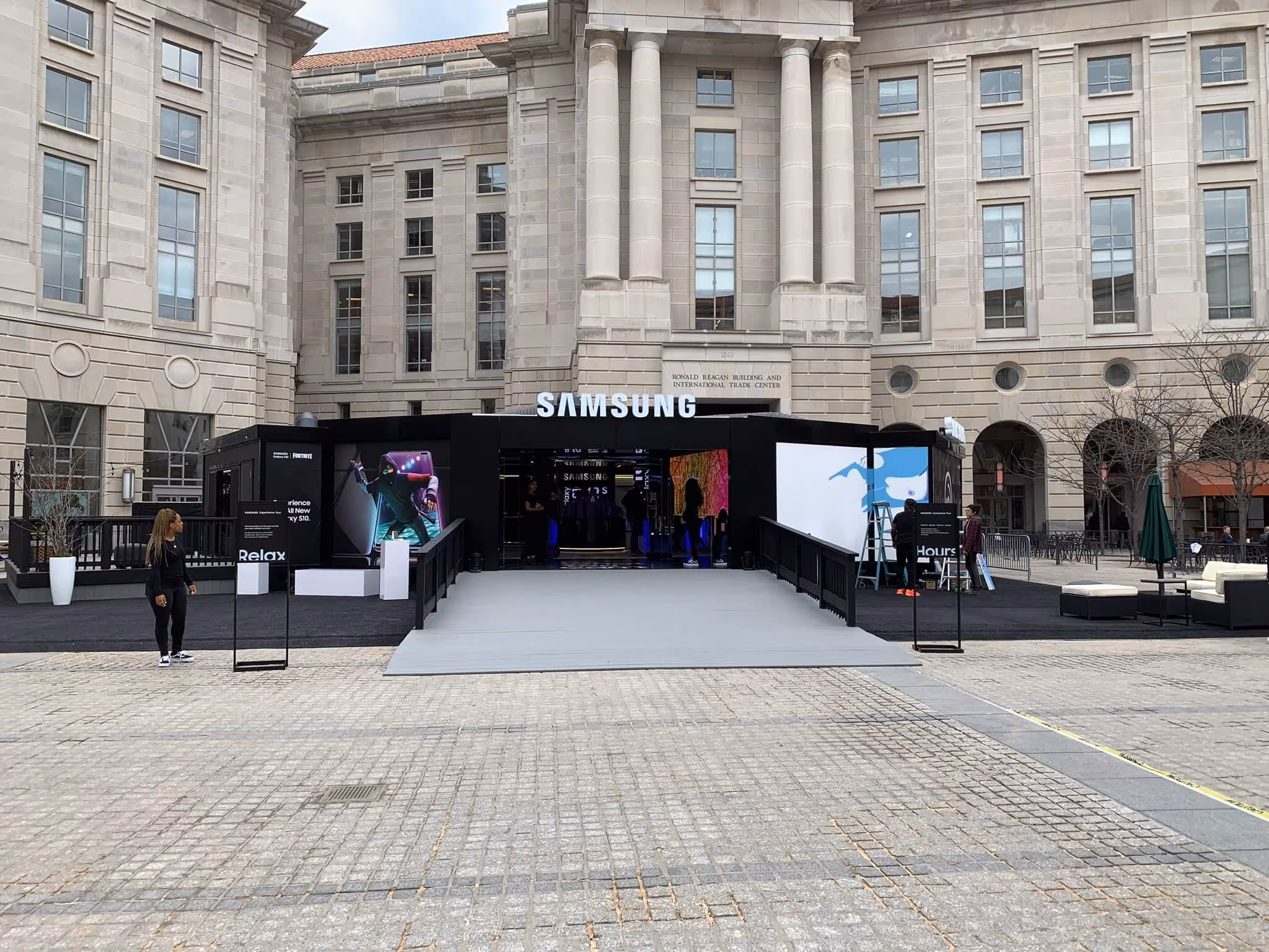 Samsung promotional booth with large screens and entrance ramp set up in front of a stone building labeled Ronald Reagan Building and International Trade Center.