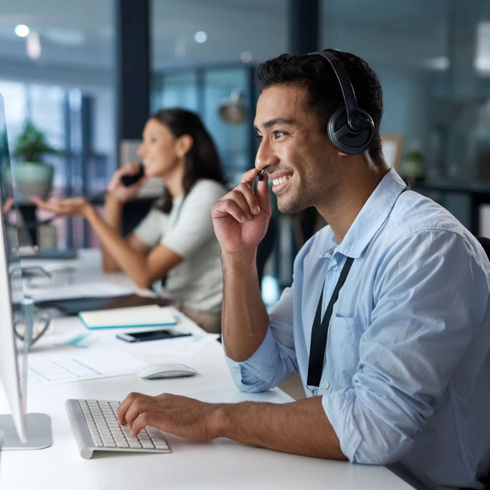 Smiling customer service representative wearing a headset and working on a computer in a modern office.