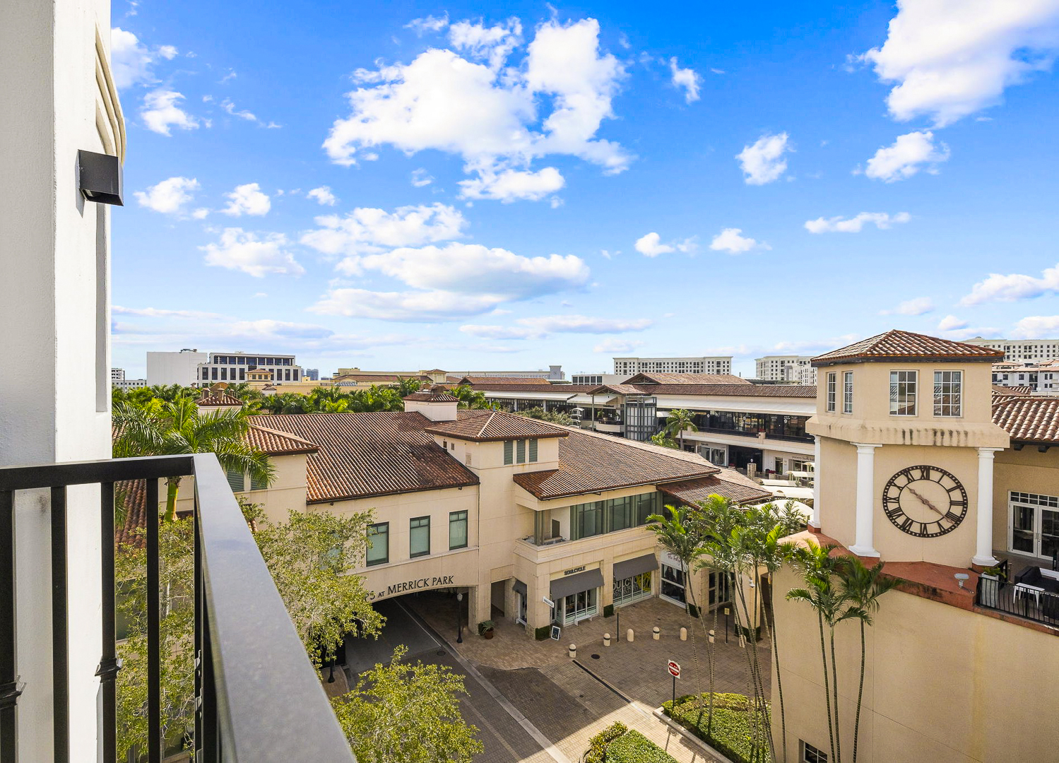 View of Shops at Merrick Park entrance from unit balcony overlooking clock tower, palm trees, and buildings of Merrick Park shopping area.