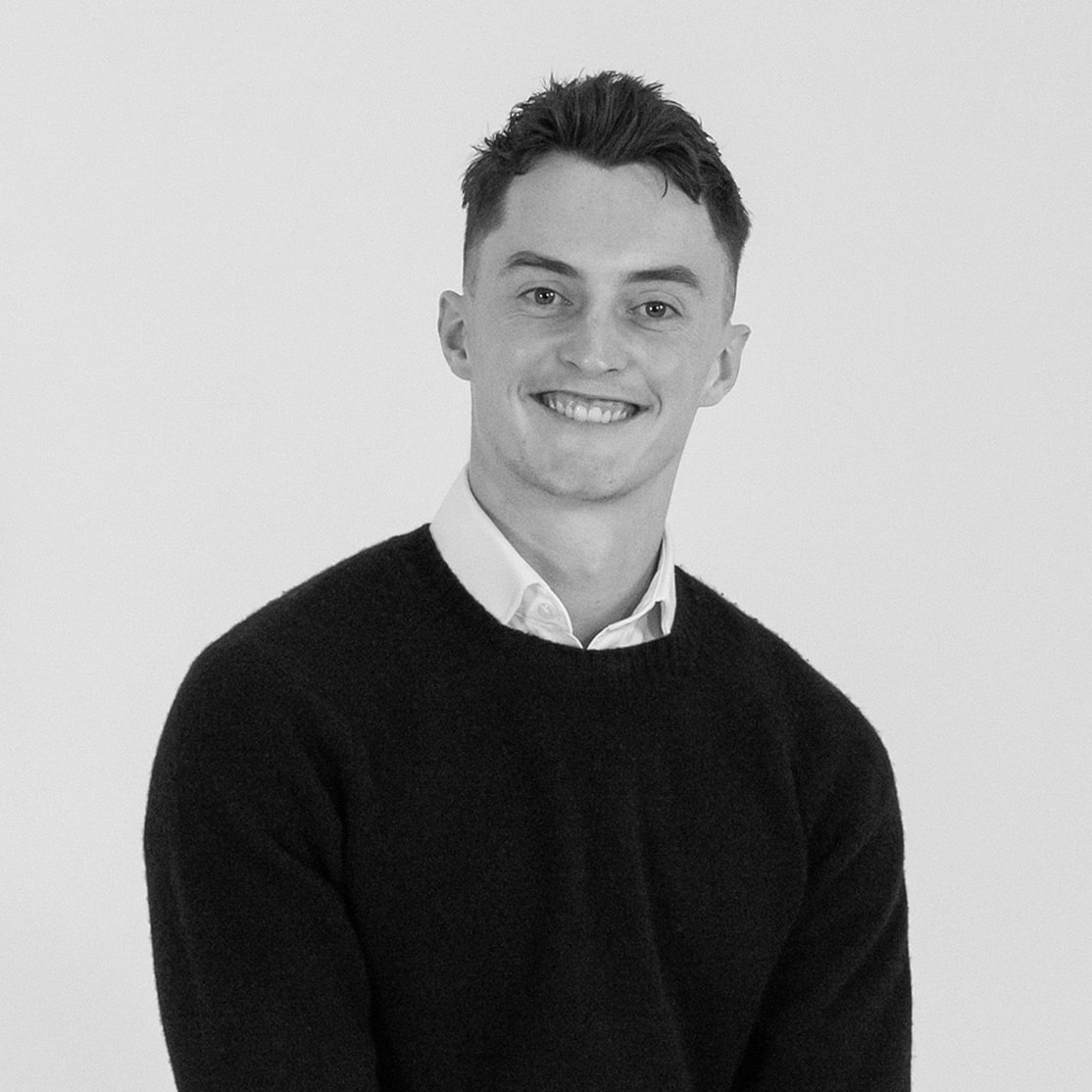 Professional portrait of senior consultant Matthew Hill smiling at the camera, wearing a dark sweater over a white collared shirt, set against a plain light background.