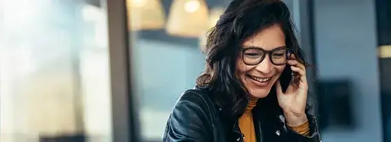 Smiling woman with glasses talking on a smartphone in an indoor setting.