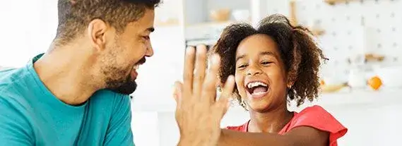 Smiling man and young girl giving each other a high-five indoors.