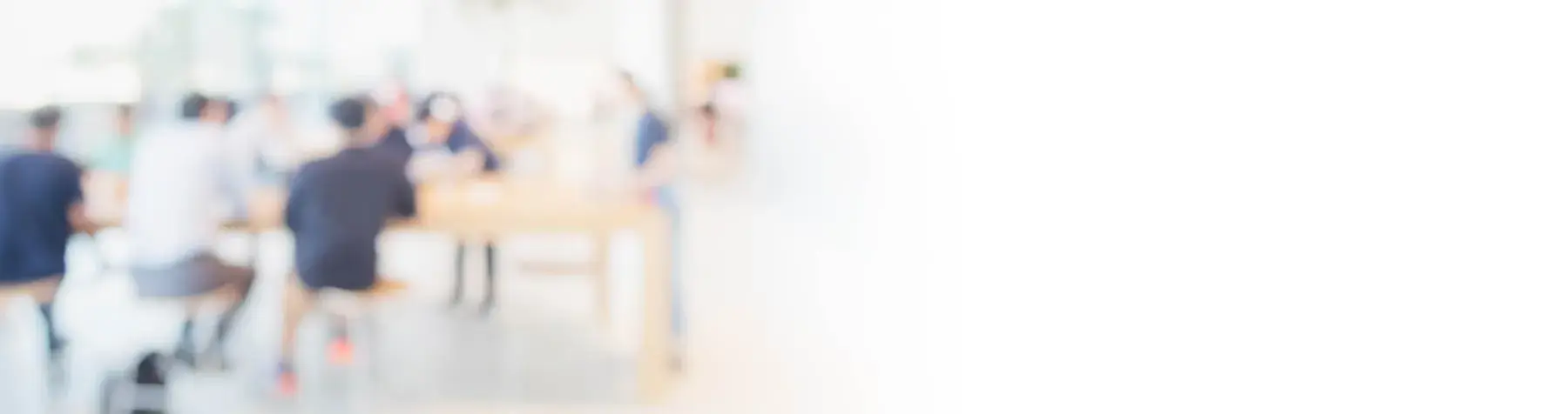 Blurred image of people sitting and interacting around a table in a bright room.