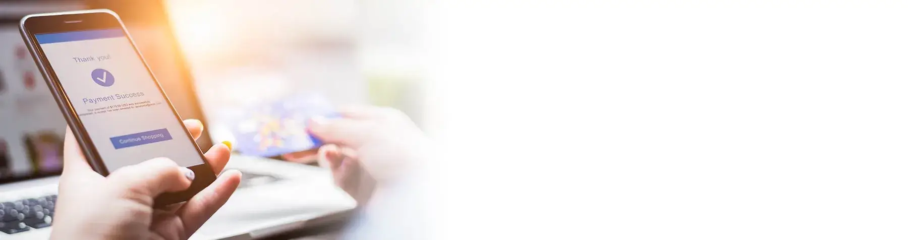 Person holding a smartphone showing a payment success confirmation and a credit card near a laptop keyboard.