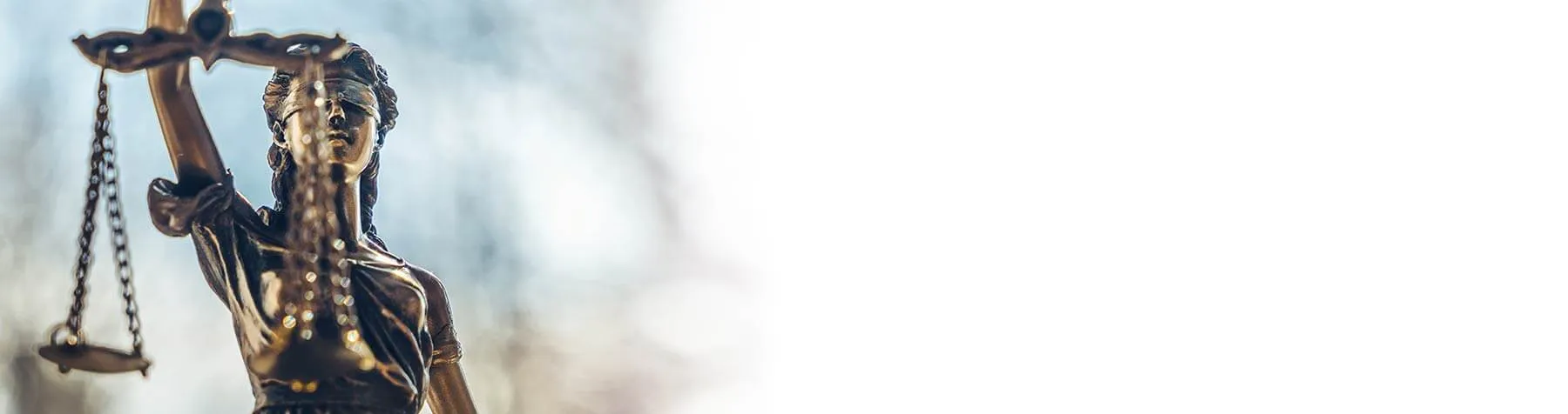 Close-up of a bronze Lady Justice statue blindfolded, holding balanced scales against a soft blurred background.