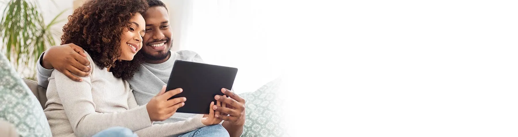 Smiling couple sitting on a couch looking at a tablet together.