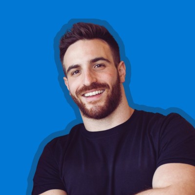 A professional headshot of Cory Blumenfeld a smiling against a blue background.
