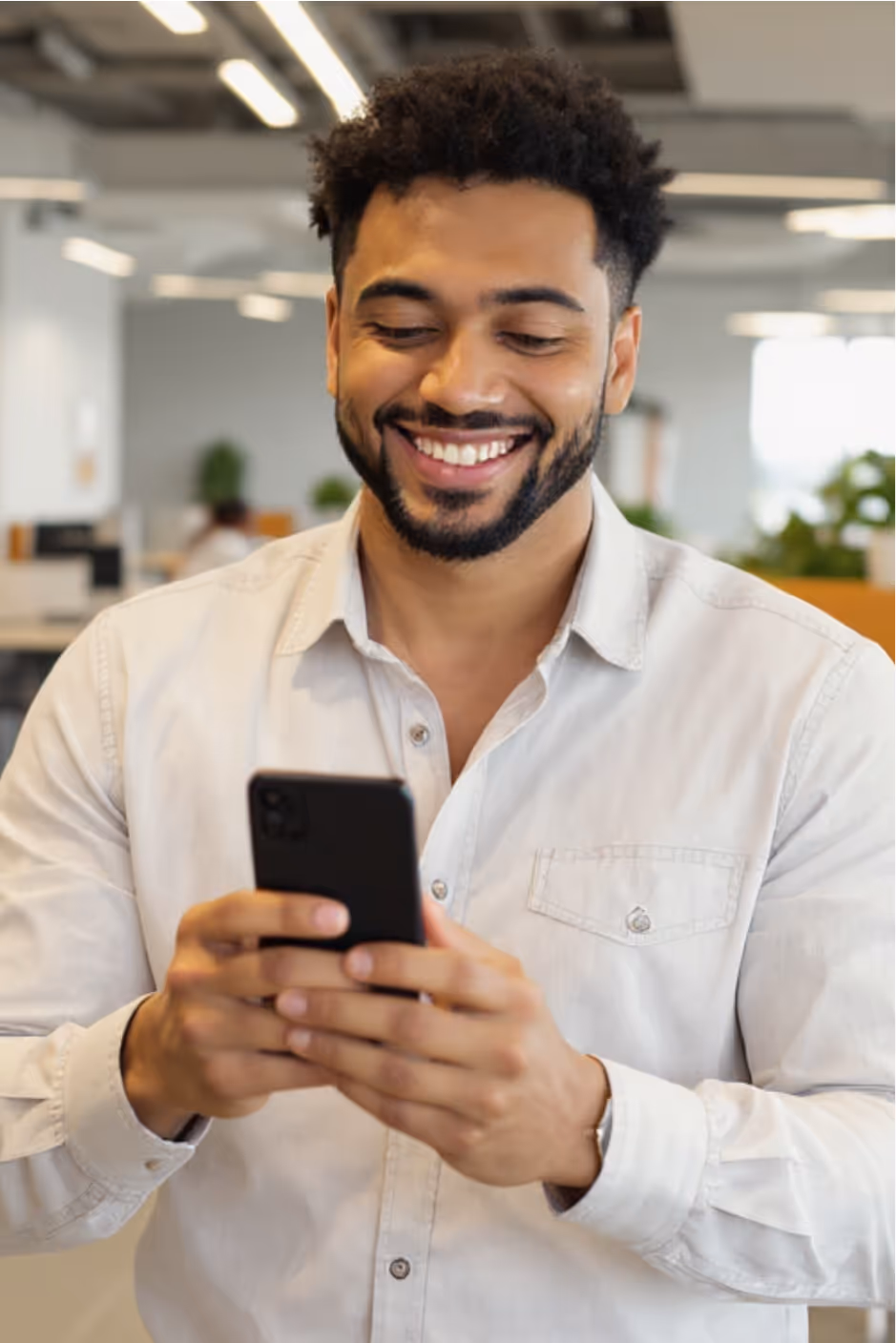 Smiling man with beard using a smartphone in a modern office.