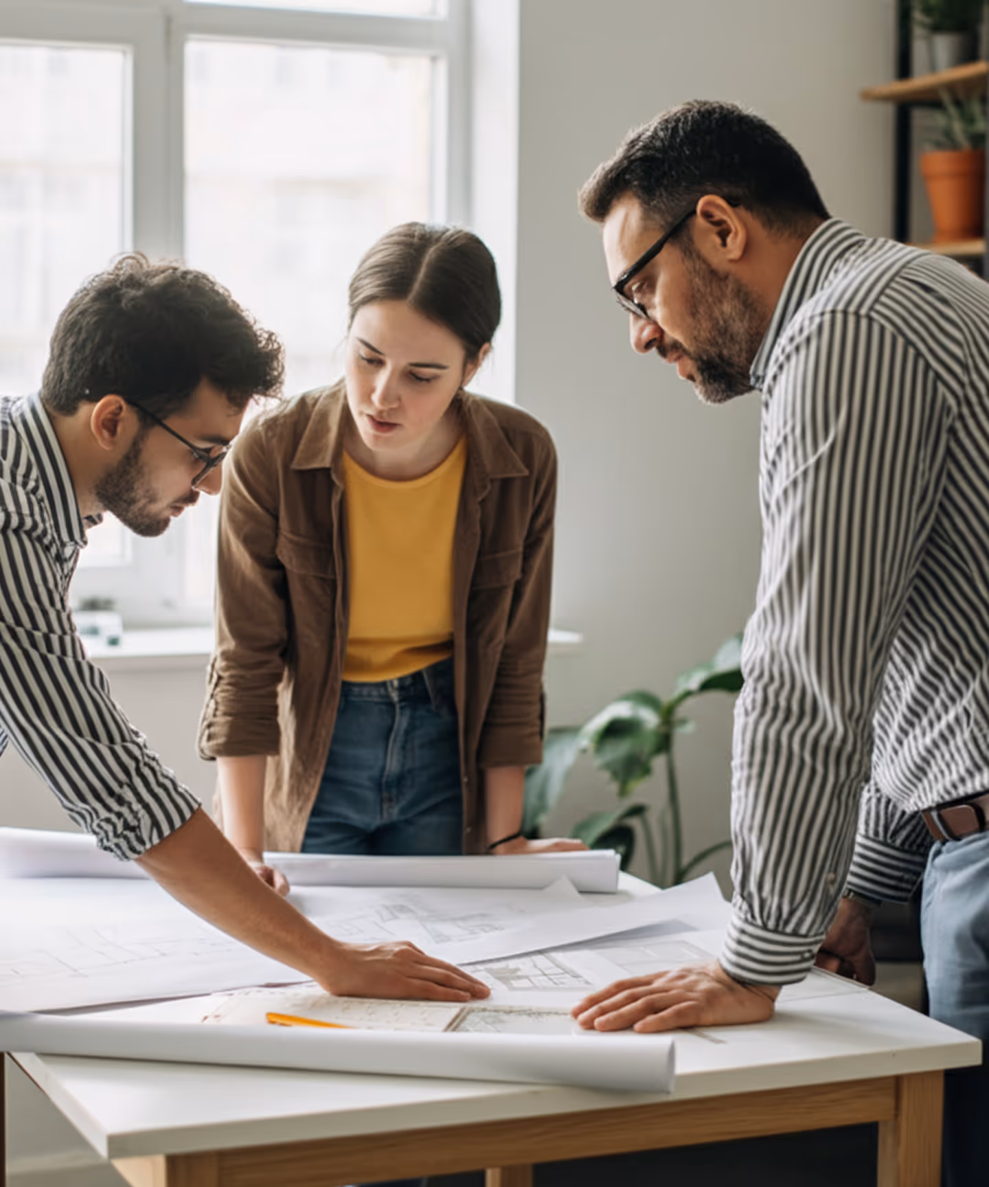Three professionals reviewing architectural blueprints on a table in a bright office.
