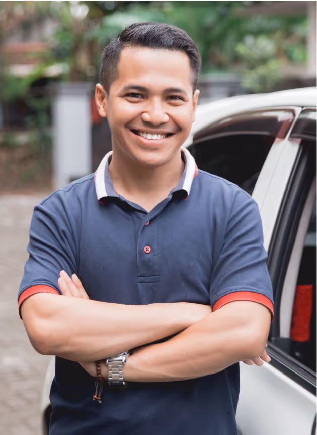 Smiling man with crossed arms standing next to a white car outdoors.