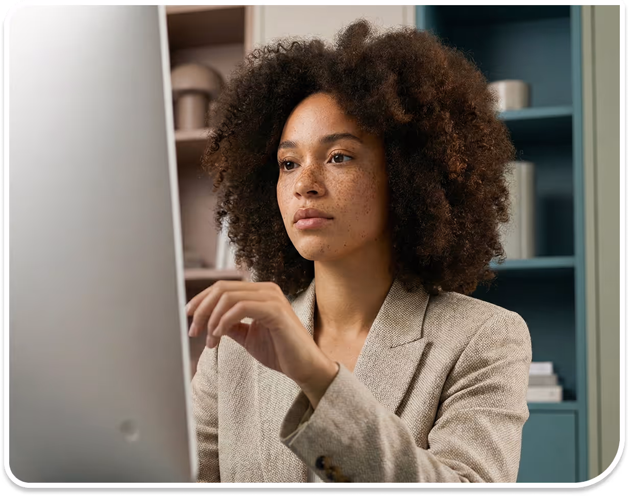 Woman with curly hair and freckles focused on a computer screen, wearing a beige blazer.