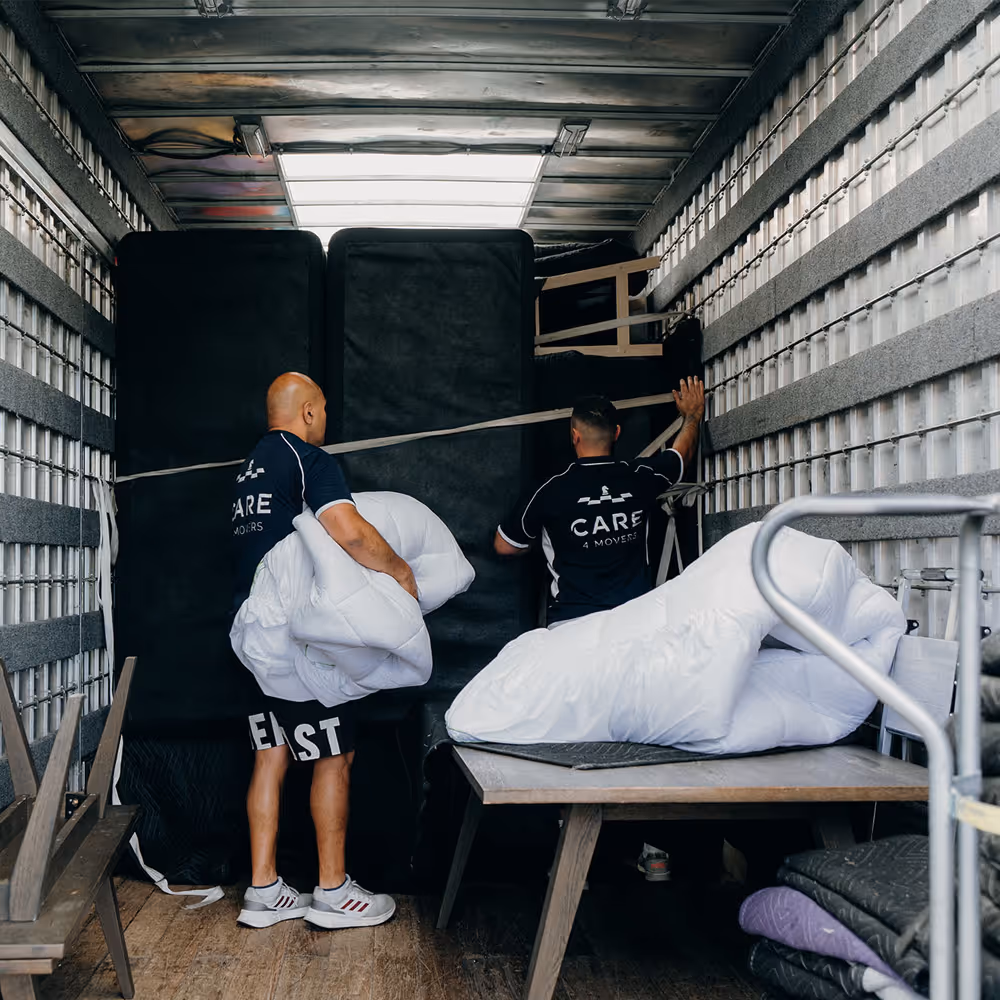 Two movers arranging black furniture and white blankets inside a moving truck.