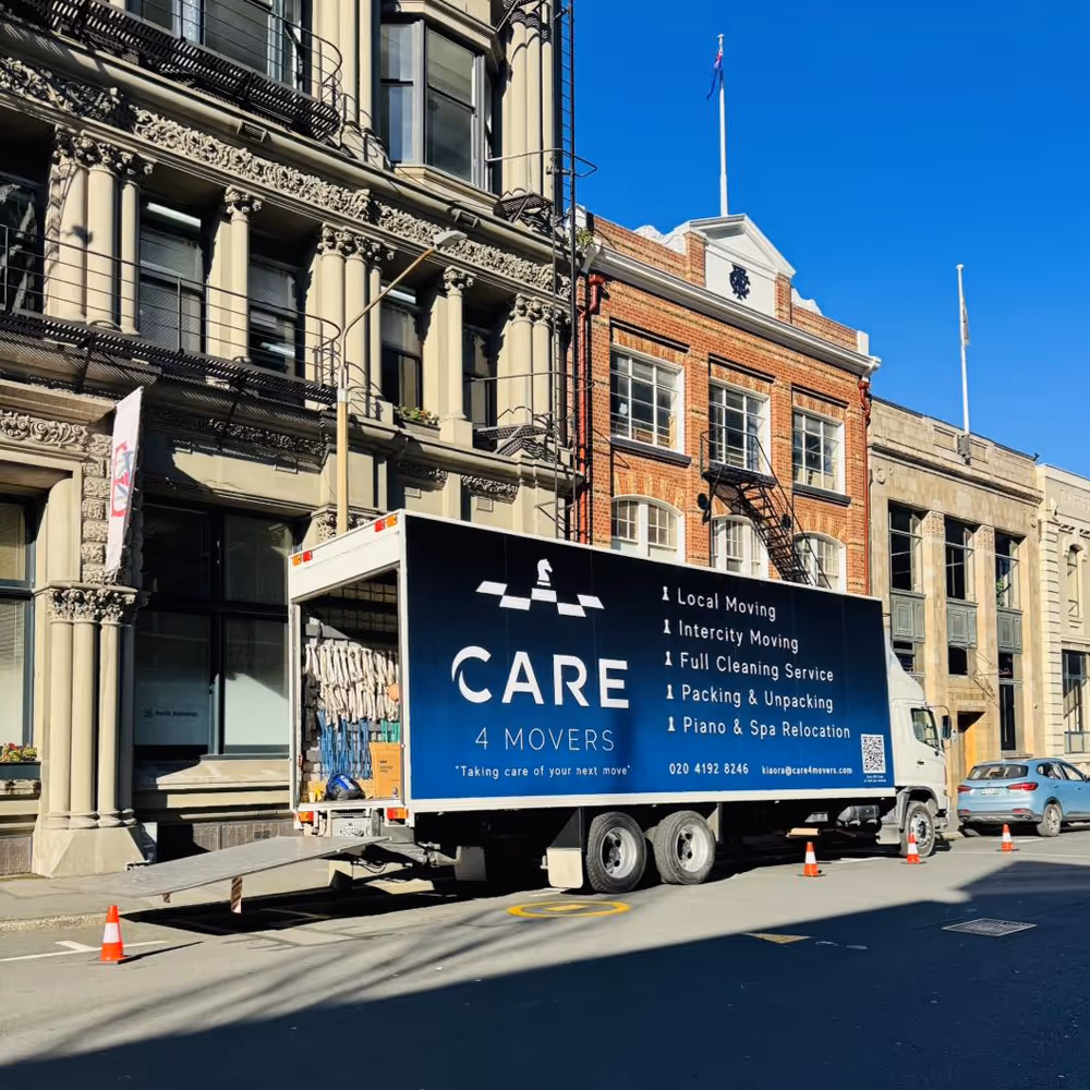 CARE 4 MOVERS truck parked on a city street with its loading ramp down, surrounded by orange traffic cones, in front of historic buildings.