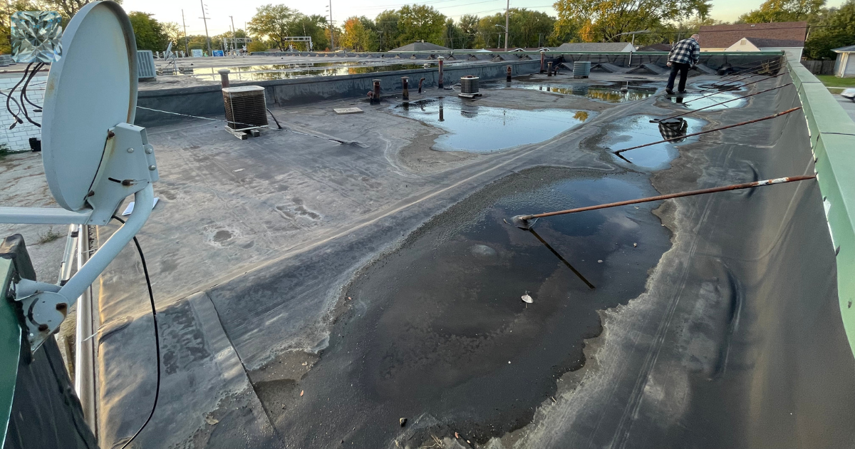 Failed commercial flat roof with ponding water and worn coating in need of inspection