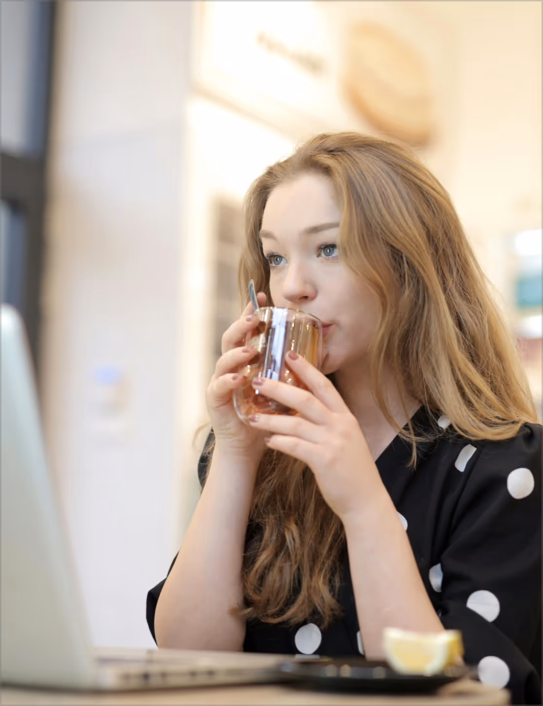 A woman drinking tea behind her laptop