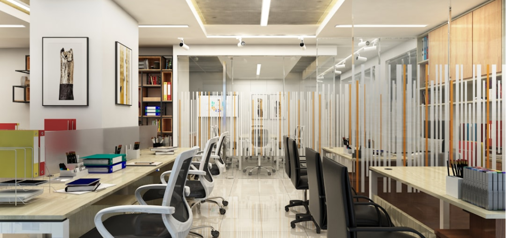 Image of an office interior with desks, chairs, and partitions.