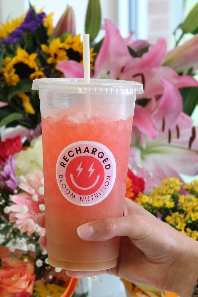 Beverage cup with straw and branding, held by hand.