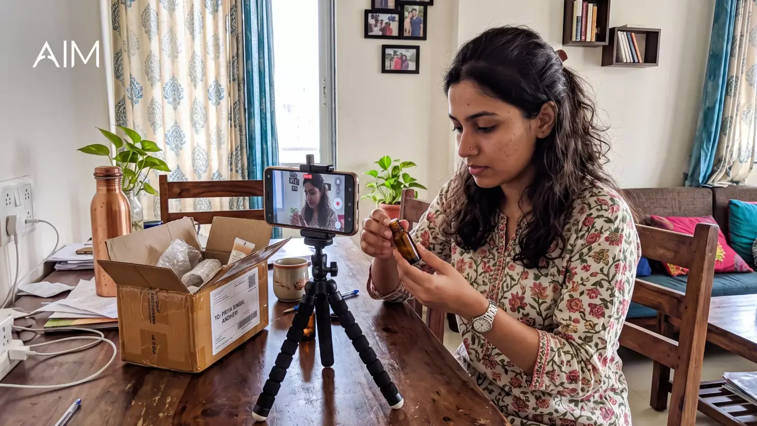 Woman filming herself on a phone tripod at home while holding a product next to an open sample box