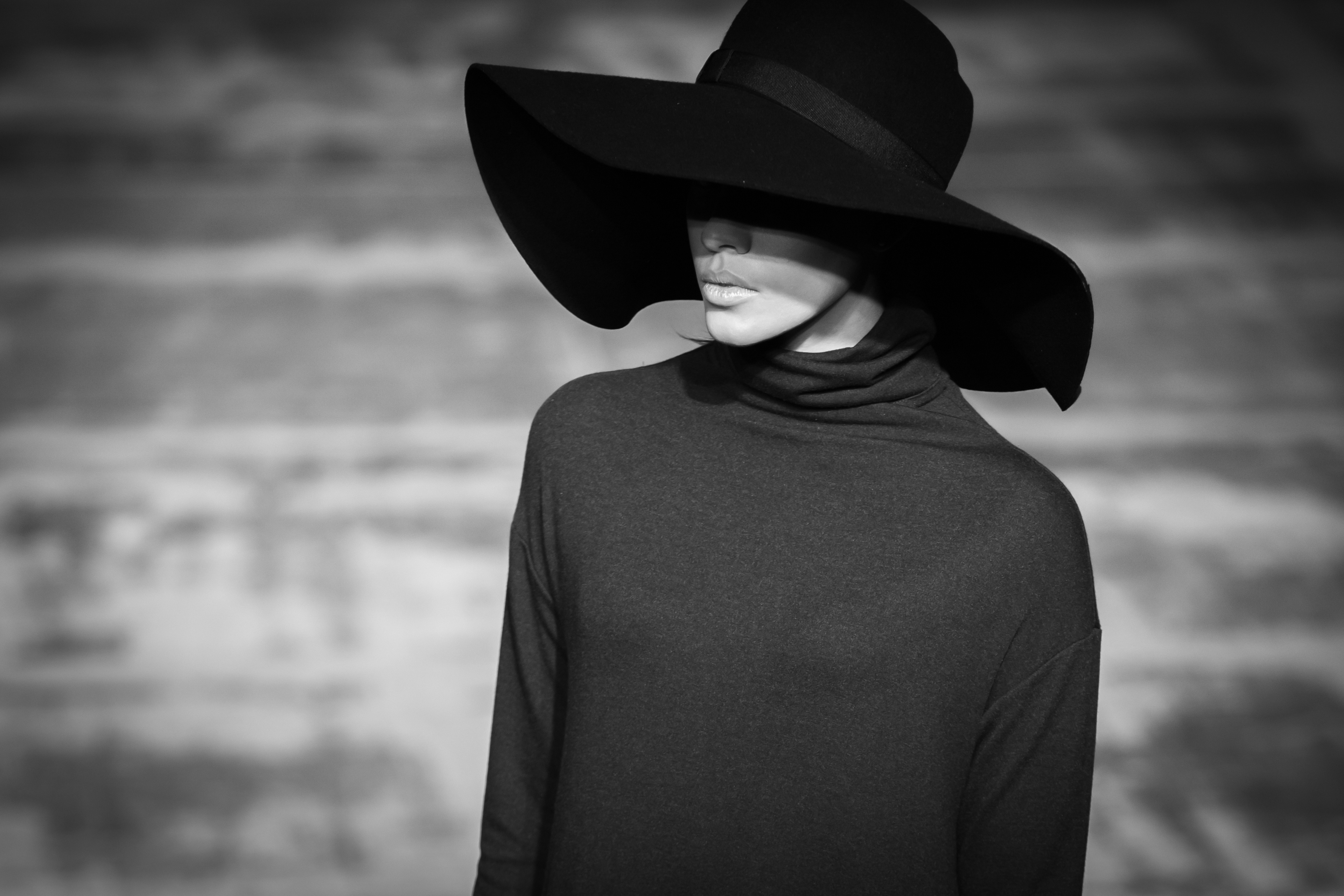 Black-and-white portrait of a woman wearing a wide-brimmed hat and a dark turtleneck sweater, with shadow covering her eyes.