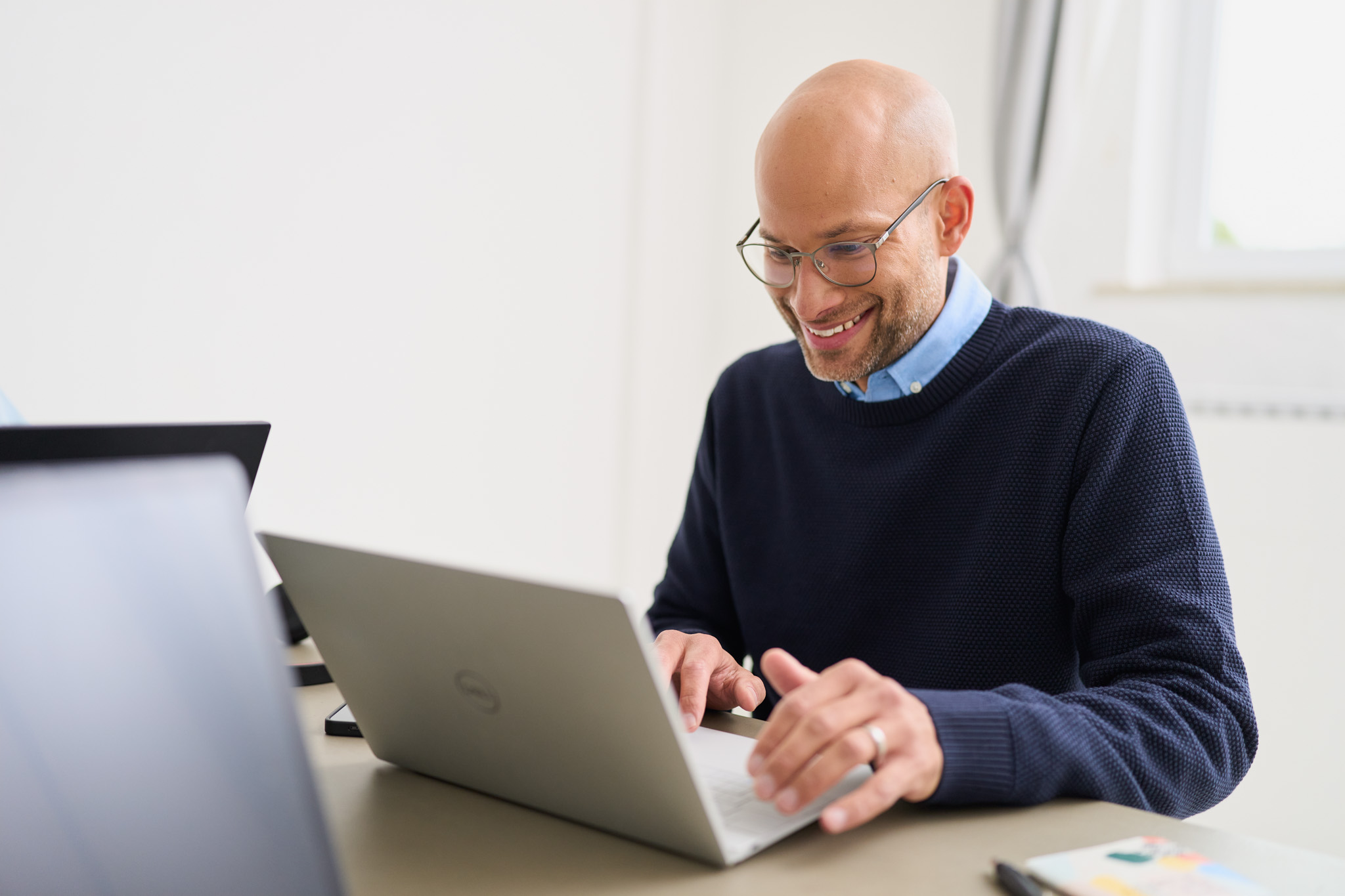 Ein Service-Mitarbeiter mit Brille von loyos bi sitzt am Laptop und lächelt.