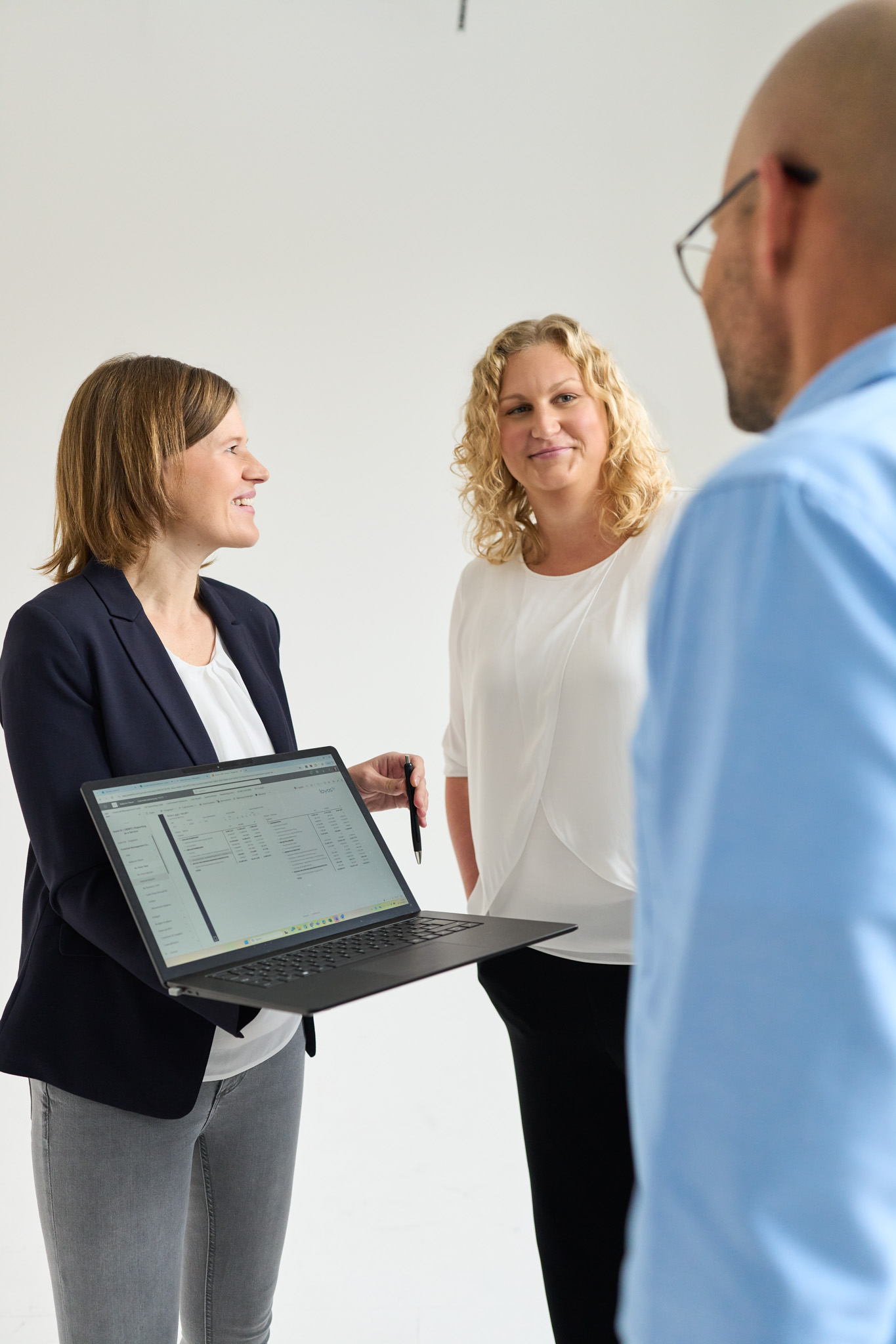 Zwei Mitarbeiterinnen von loyos bi zeigen einem Kollegen etwas auf einem Laptop.