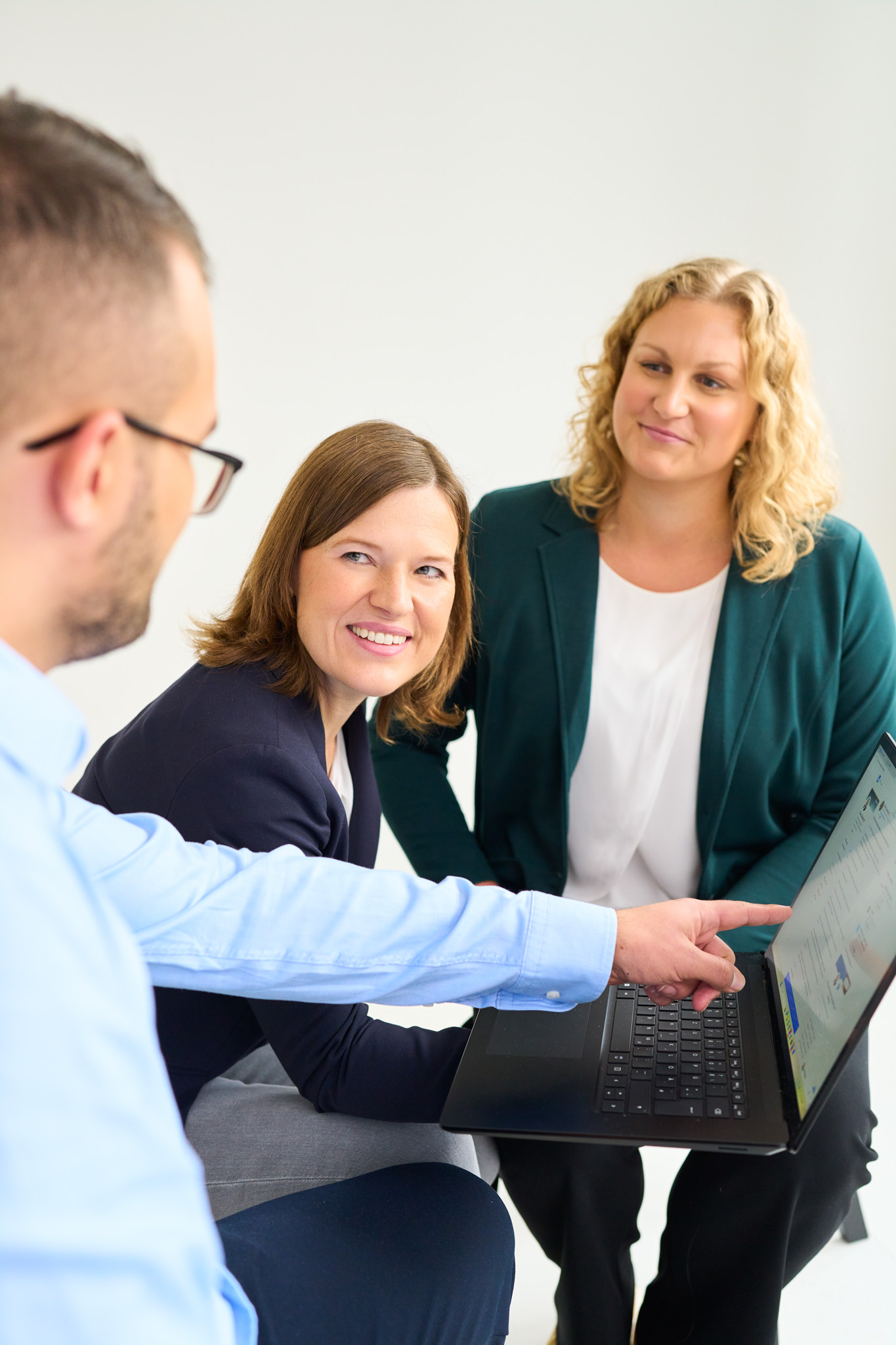 Zwei Kolleginnen von loyos bi lächeln Ihren Kollegen an, er zeigt etwas auf dem Laptop.