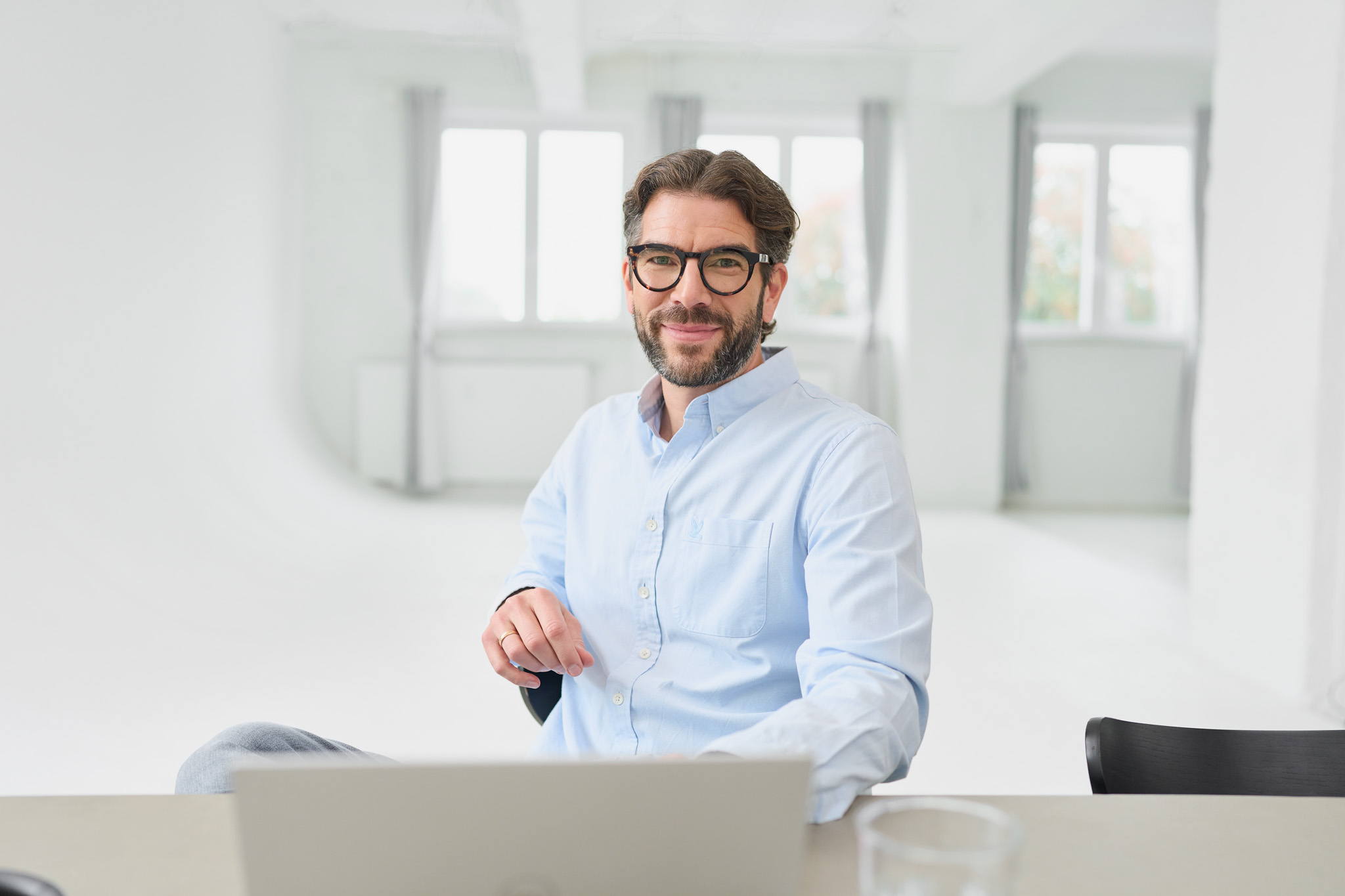 Martin Sperling von loyos bi lächelt in die Kamera, sitzt vor seinem Laptop.