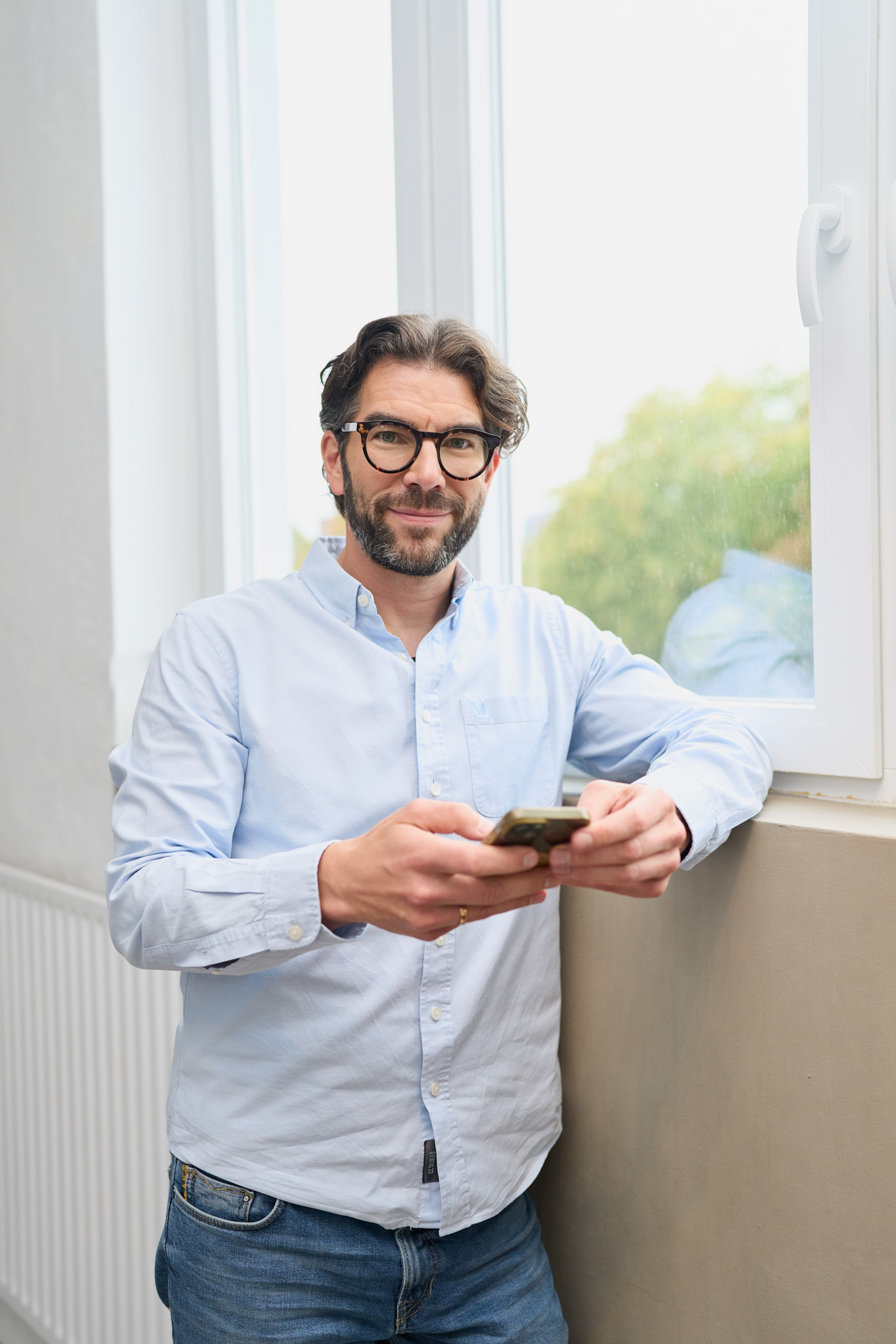 Martin Sperling von loyos bi lächelt in die Kamera, hat ein Handy in beiden Händen.