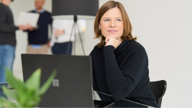 Eine Frau mit braunem Haar arbeitet bei loyos bi, sie schaut verträumt zur Seite, vor sich der Laptop.