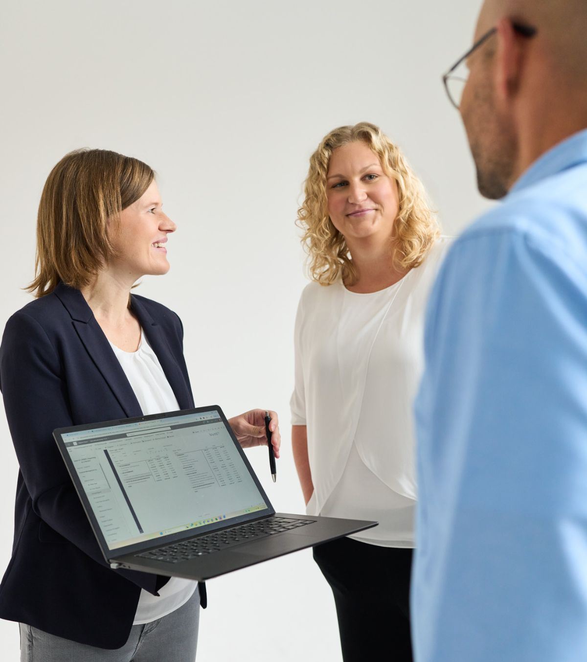 Zwei Frauen und ein Mann stehen, ein Laptop in der Mitte, sie unterhalten sich und lächeln. Sie arbeiten bei loyos bi.