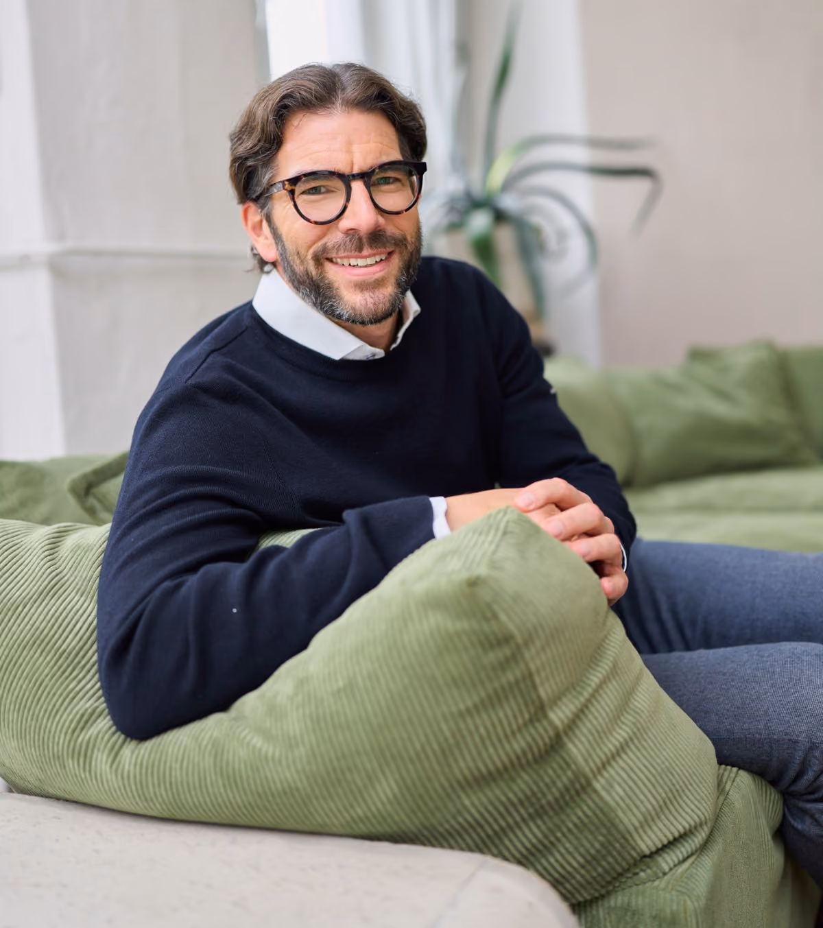 Der Geschäftsführer von loyos bi sitzt auf einer grünen Couch, lächelt in die Kamera.