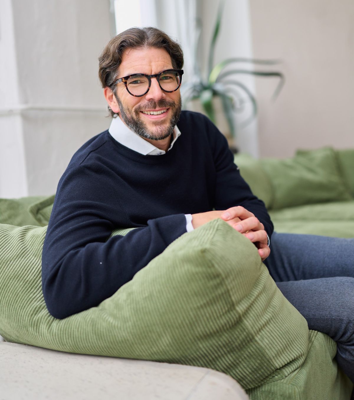 Der Geschäftsführer von loyos bi sitzt auf einer grünen Couch, lächelt in die Kamera.