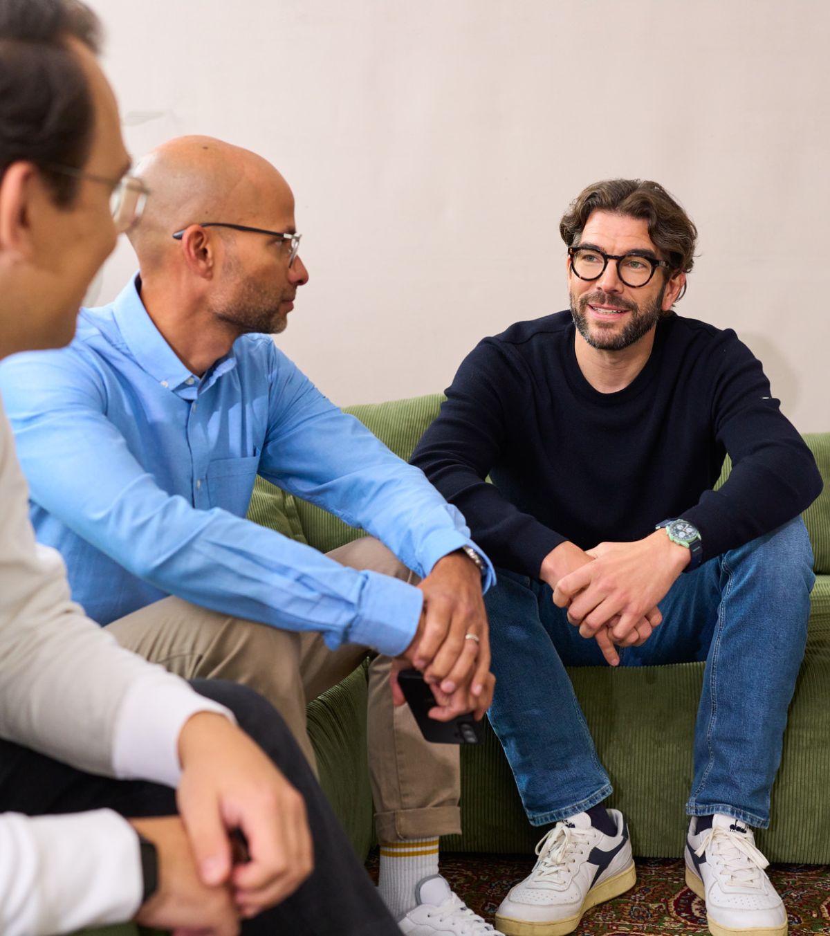 Drei Männer die bei loyos bi arbeiten sitzen auf einer Couch, unterhalten sich, zwei sieht man nur von hinter oder von der Seite.