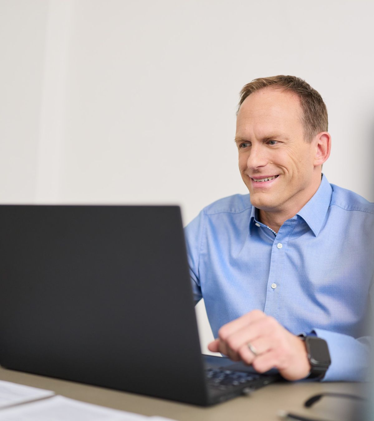 Ein Mann von loyos bi sitzt am Laptop, lächelt, schaut auf den Laptop.