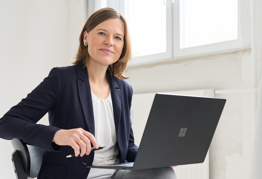 Eine Kollegin von loyos bi sitzt, ihr aufgeklappter Laptop vor sich, Sie lächelt in die Kamera.