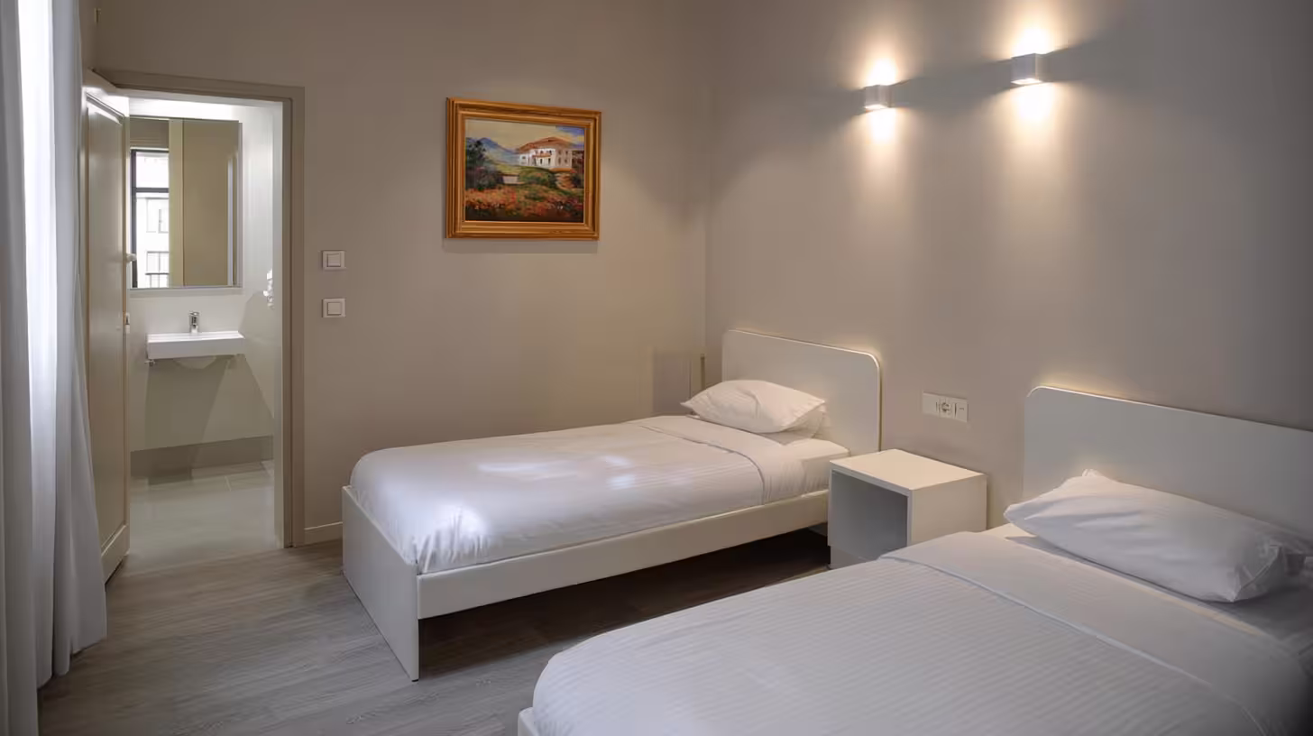 Chambre twin de l’Hôtel des Arceaux, deux lits simples avec éclairage mural et accès direct à la salle d’eau privée.