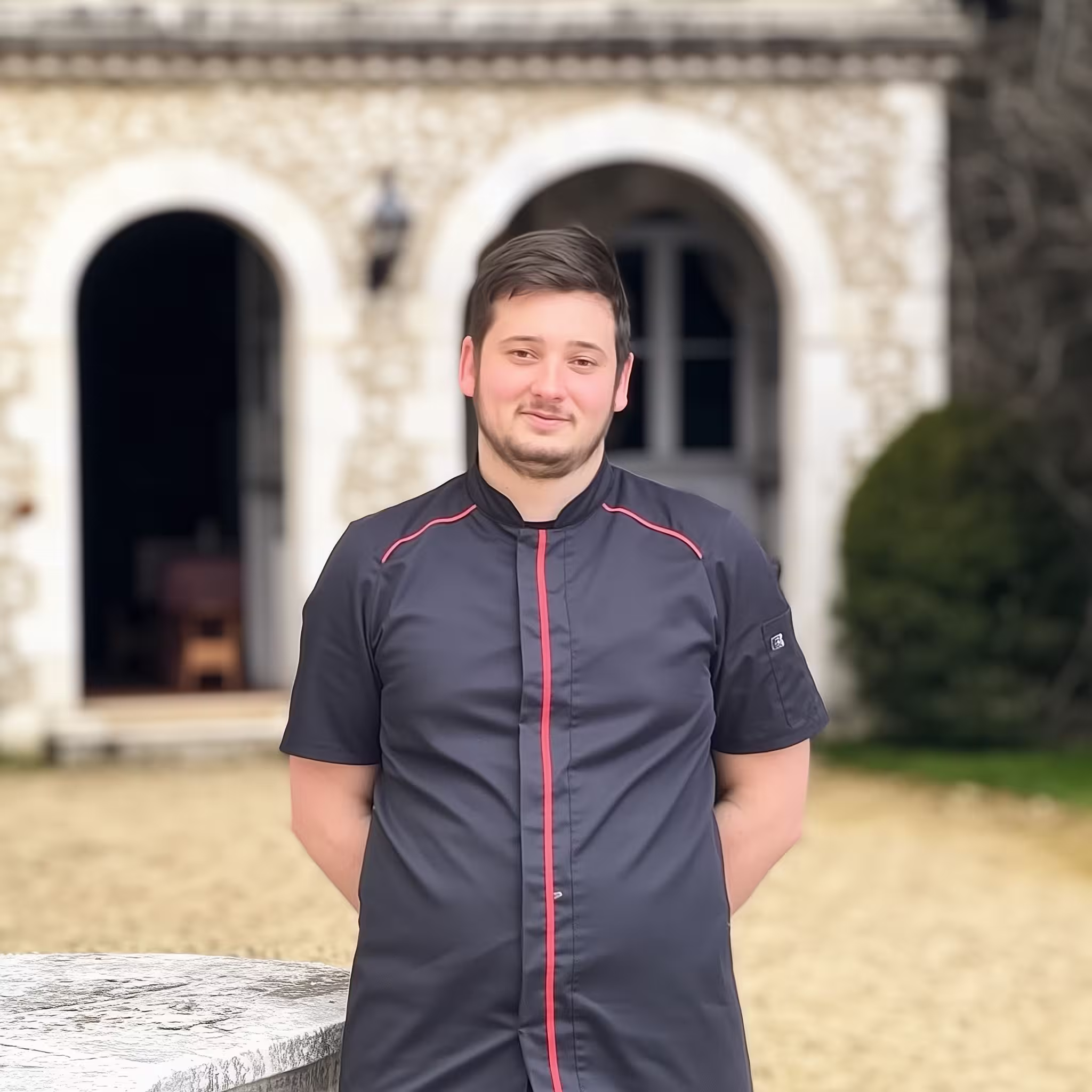 Portrait de Damien, chef de cuisine du Bistrot des Arceaux, vêtu d’une veste noire à liseré rouge.