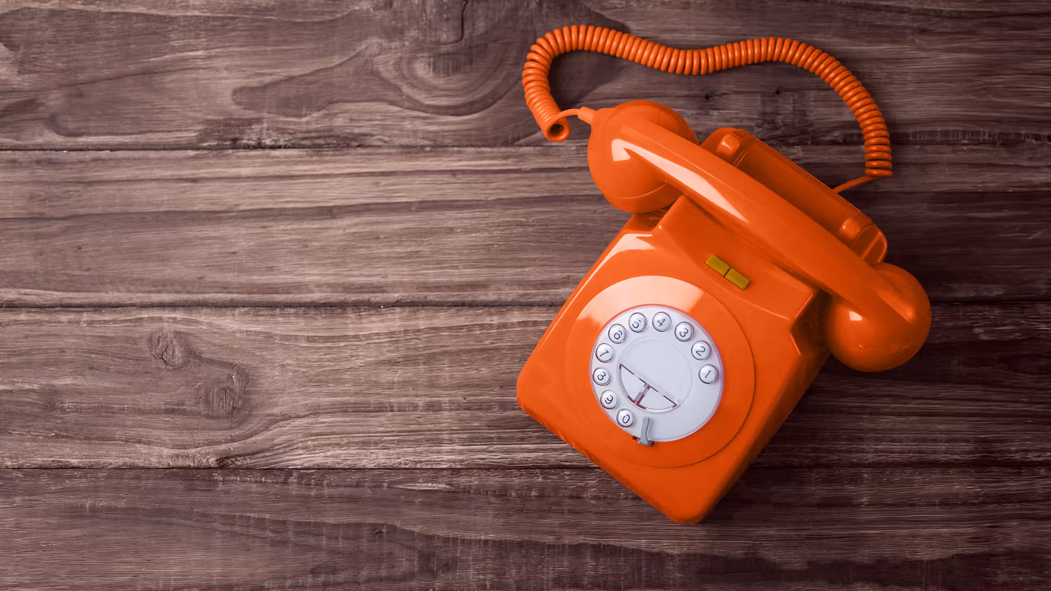 Téléphone vintage orange sur fond en bois, symbole du contact chaleureux du Bistrot des Arceaux.