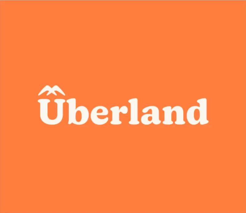Weißes Logo 'Überland' mit stilisierten Berggipfeln über dem Umlaut auf orangefarbenem Hintergrund.
