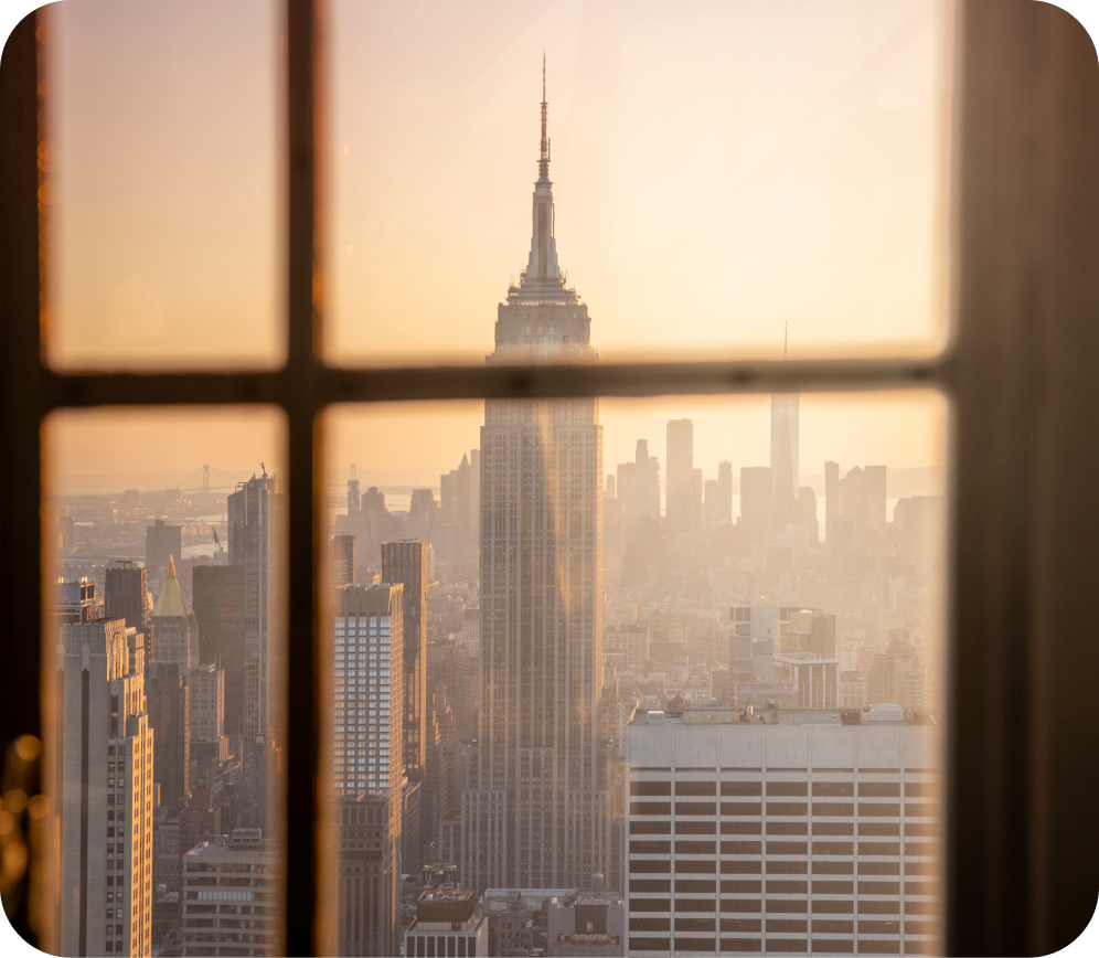 View of the Empire State Building and New York City skyline at sunset through a window with crossbars.