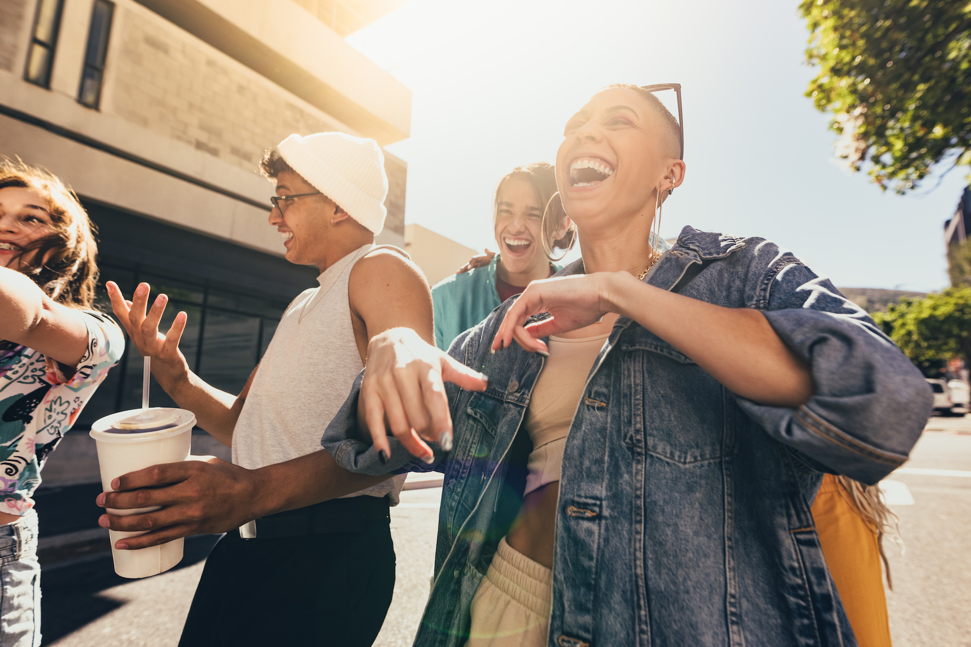 Group of diverse young friends laughing and having fun outdoors on a sunny day.
