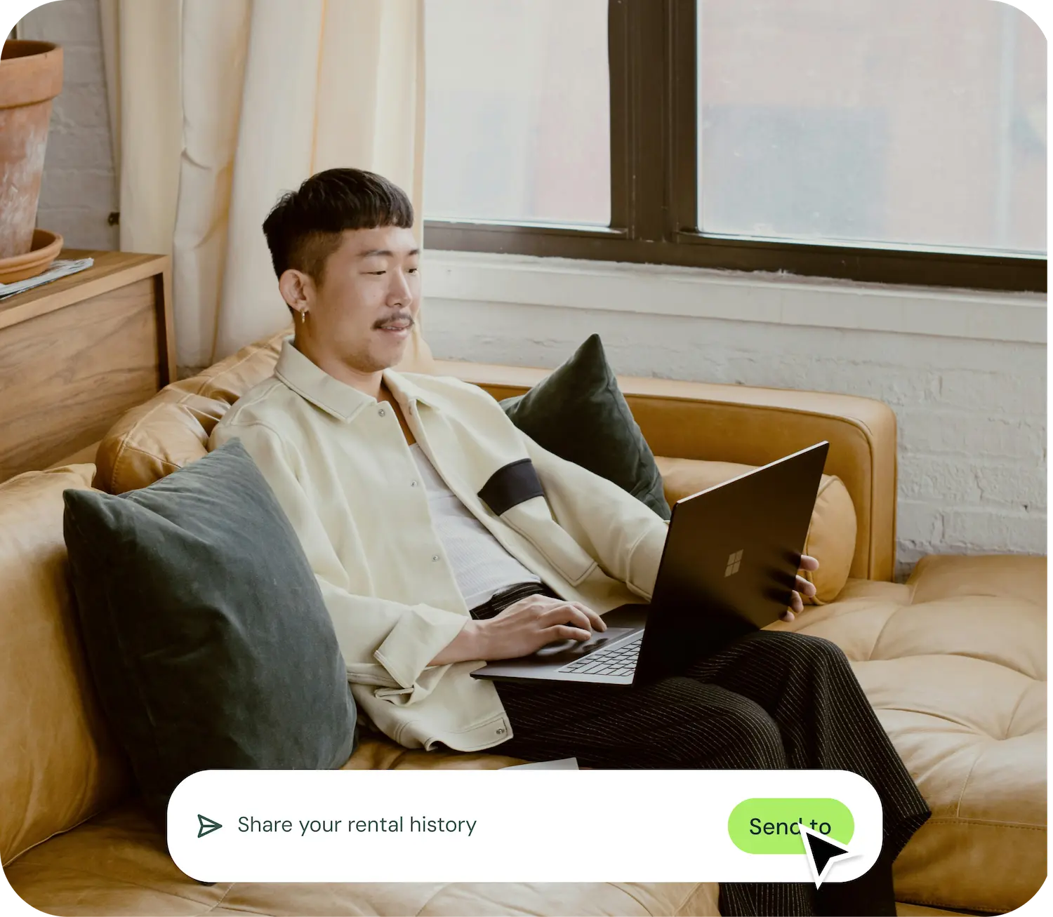 Man sitting on a tan leather couch using a laptop with a text overlay button that says 'Share your rental history' and 'Send to'.