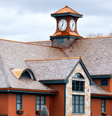 Building with a clock tower, featuring a copper roof, stone accents, and a multi-peaked roofline.