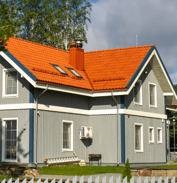 Two-story gray house with white trim, an orange tile roof, and a small white fence in the foreground.
