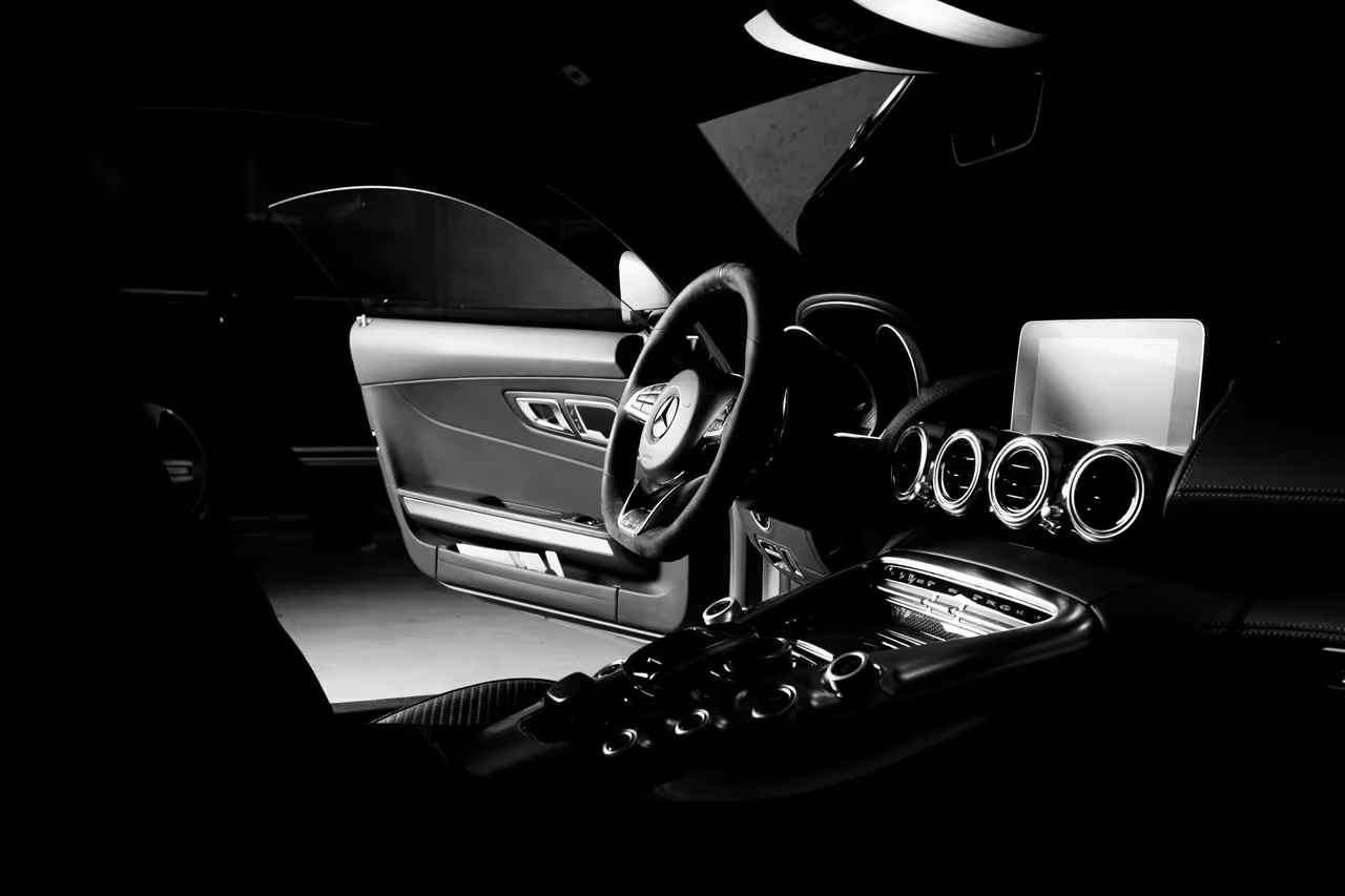 Interiør av luksuriøs bil med Mercedes-ratt, åpnet dør, sirkulære luftdyser og digital skjerm på dashbordet.